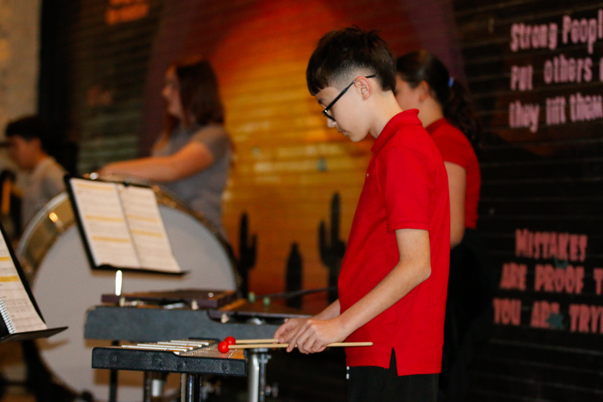 A preteen boy in glasses and a red t-shirt plays xylophone