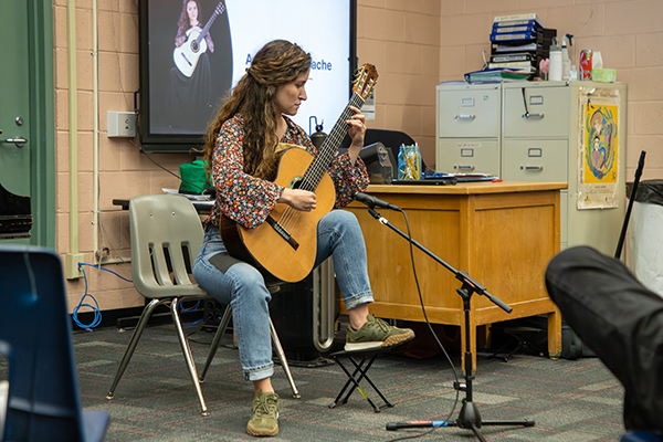 A woman plays guitar in a middle school class