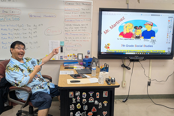A man in a Hawaiian shirt excitedly points at his SmartBoard screen, with a cartoon image on it