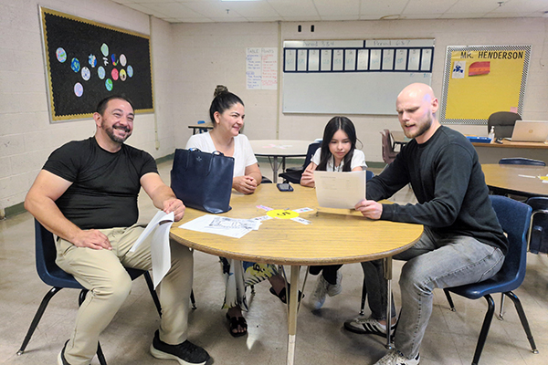 A dad, mom and daughter sit at a table with the daughter's teacher