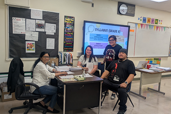 A family sits around their child's teacher's desk